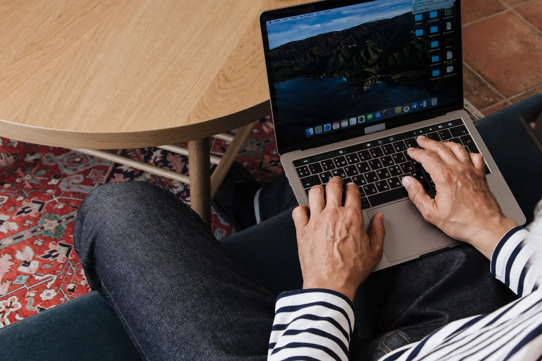 Close up of hands typing on a laptop keyboard surrounded by study notes on a wooden desk