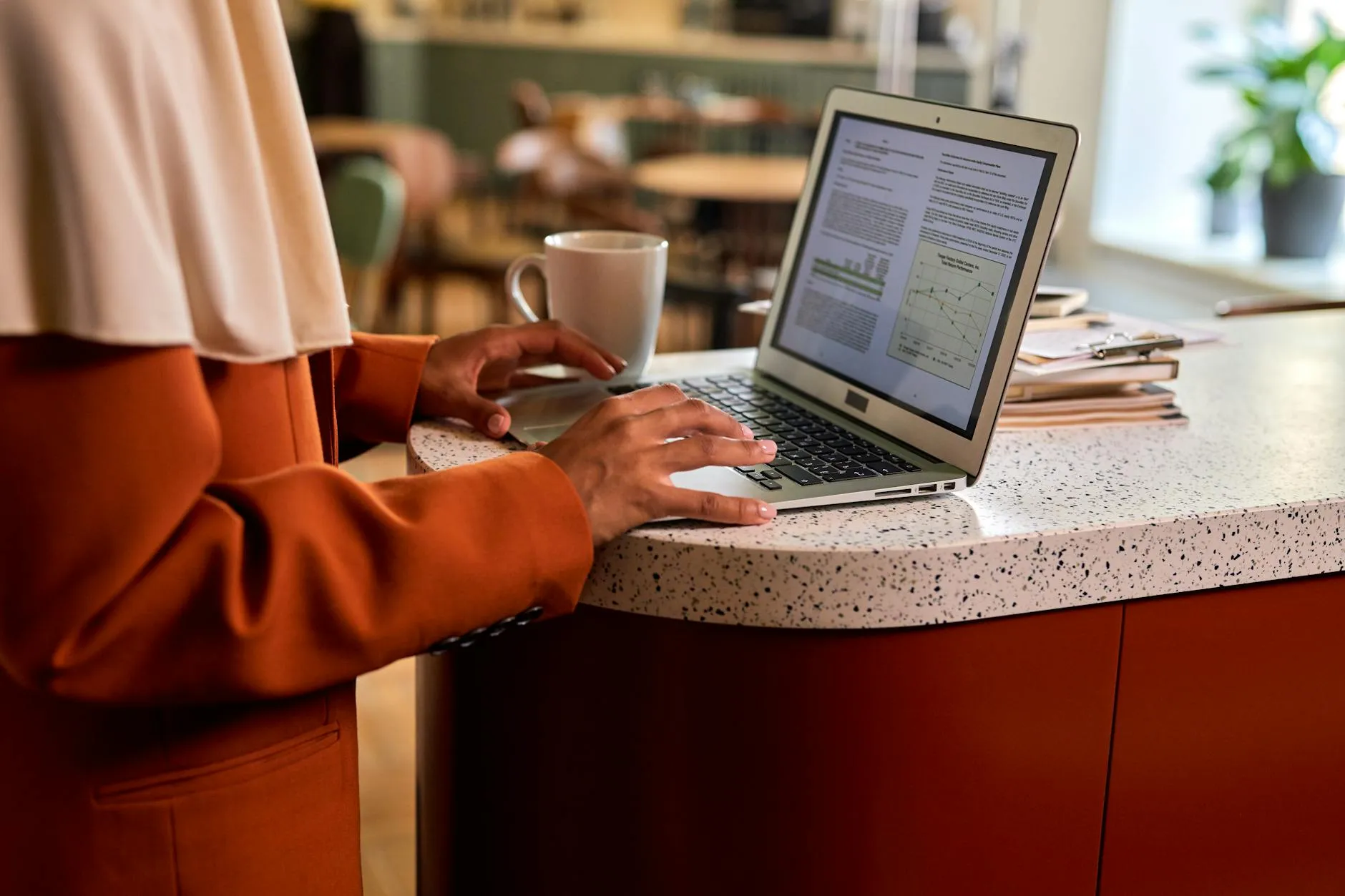 Close up of hands typing on a laptop on a messy student desk with a coffee mug and notebooks