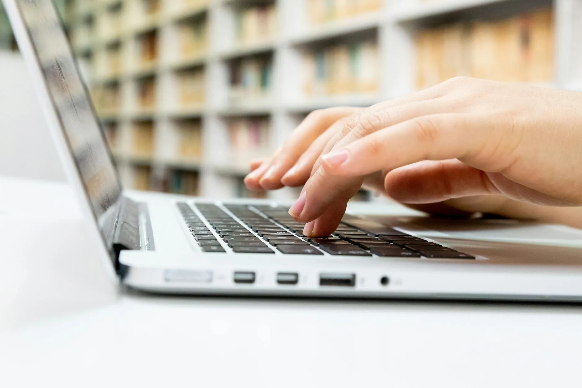 Close up of a student hands typing on a laptop with stickers in a modern university library
