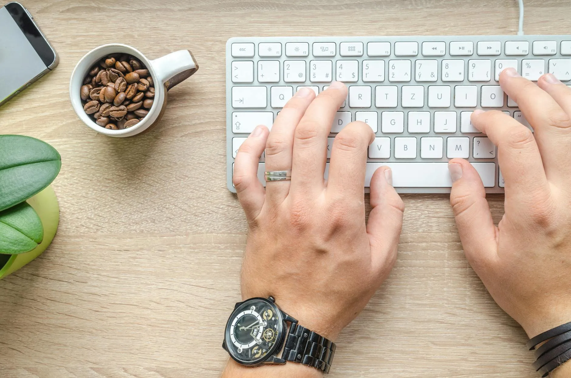 Close up of hands typing on a laptop on a messy study desk with a coffee cup nearby