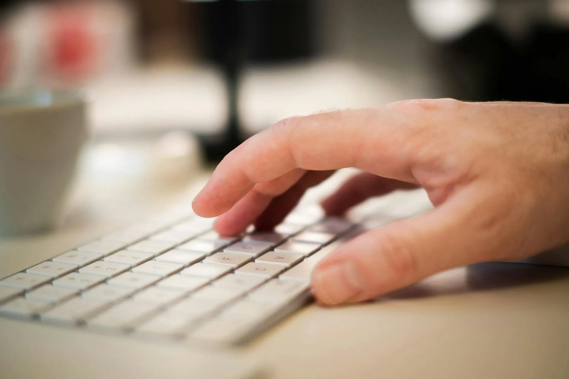 Close up of hands typing on a laptop next to a tablet on a messy study desk with coffee