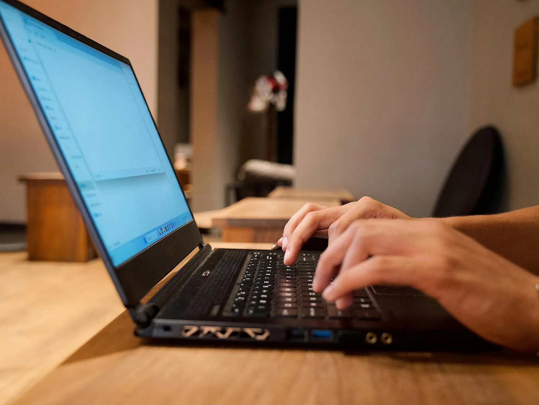Close up of a student typing on a laptop at a messy dorm desk with a hydroflask and stickers