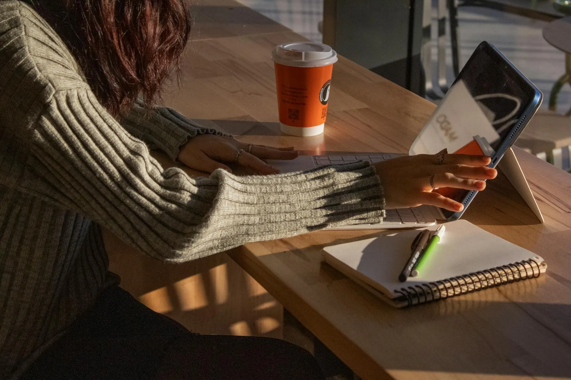 Close up of a students hands using a tablet for digital note taking in a sunlit coffee shop