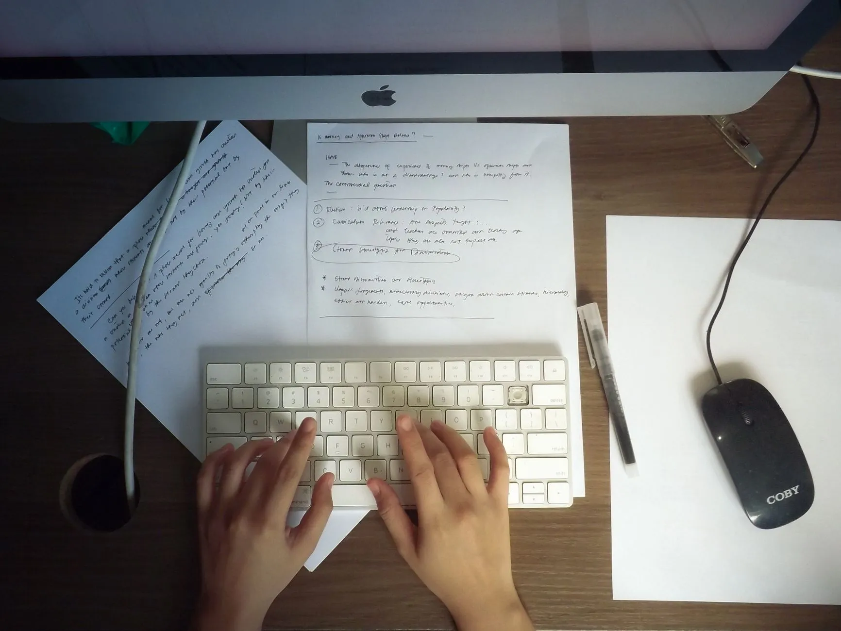 Close up of hands typing on a laptop keyboard surrounded by handwritten study notes and a coffee cup