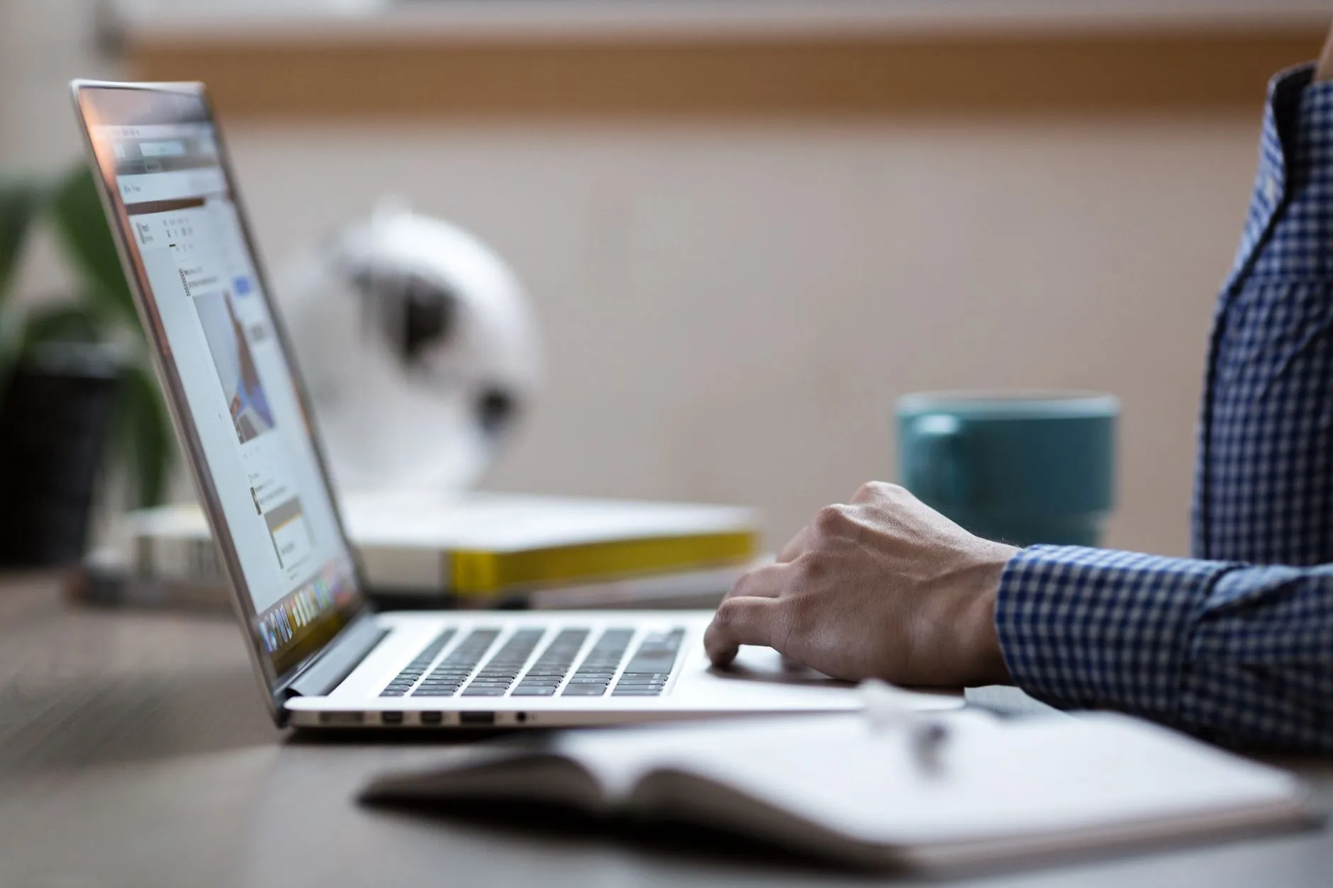 Close up of hands typing on a laptop next to an open notebook on a messy study desk