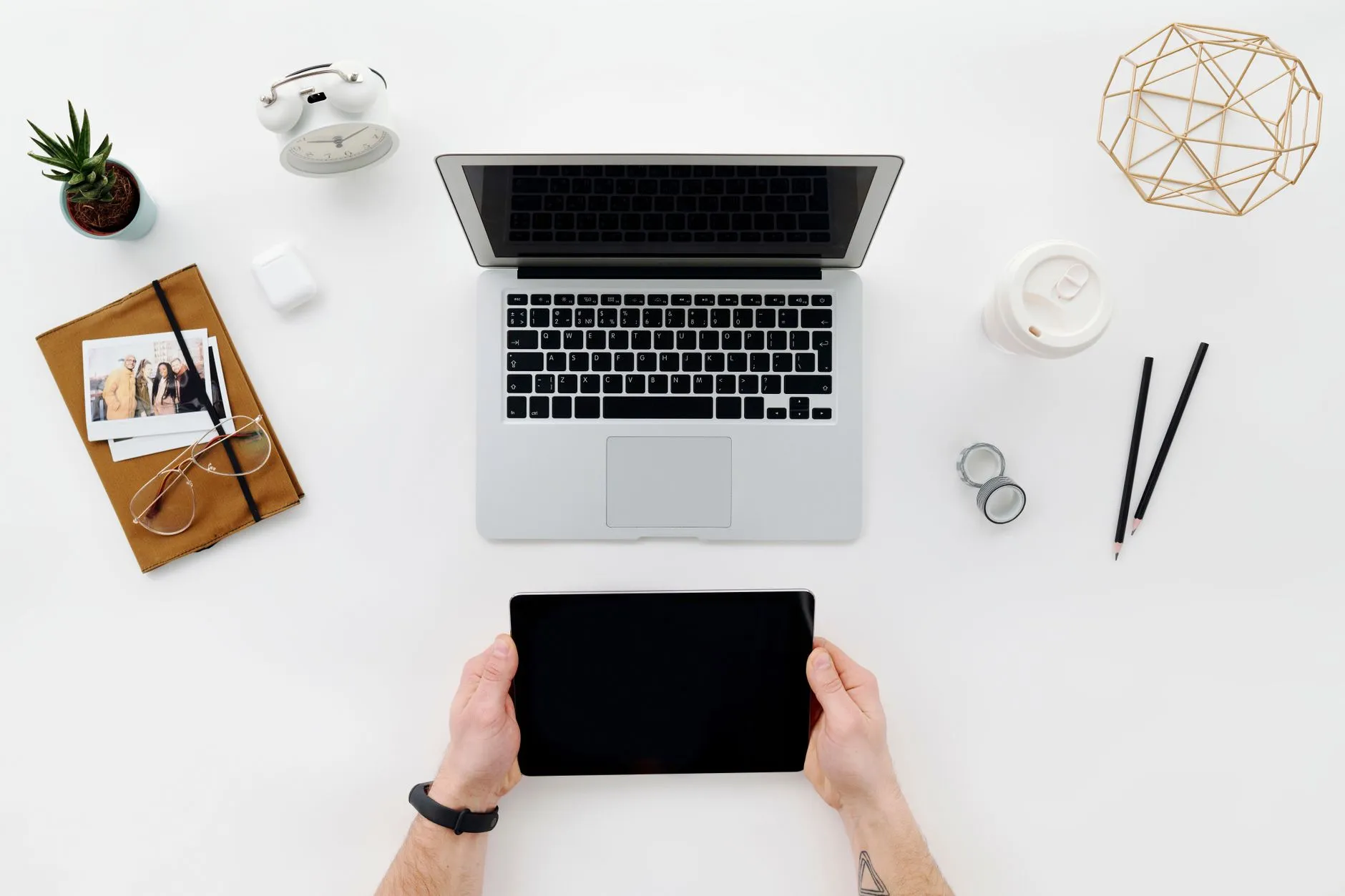 Close up of hands typing on a laptop next to a tablet displaying digital flashcards on a messy student desk