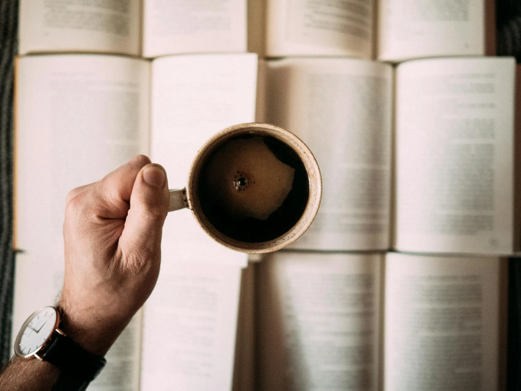 Close up of a student holding a warm mug at a messy study desk filled with notebooks and a laptop