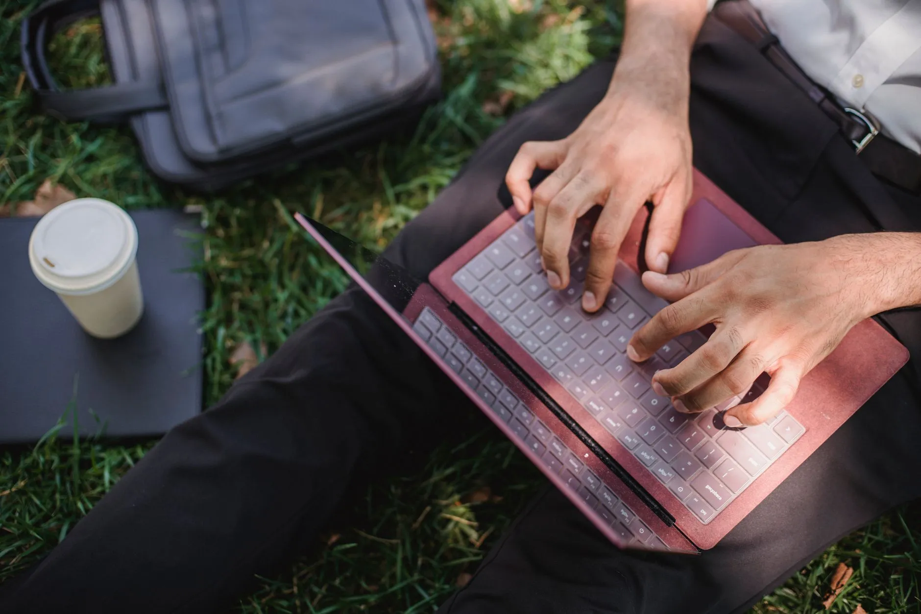 Close up of hands typing on a laptop on a messy student desk with a coffee cup nearby
