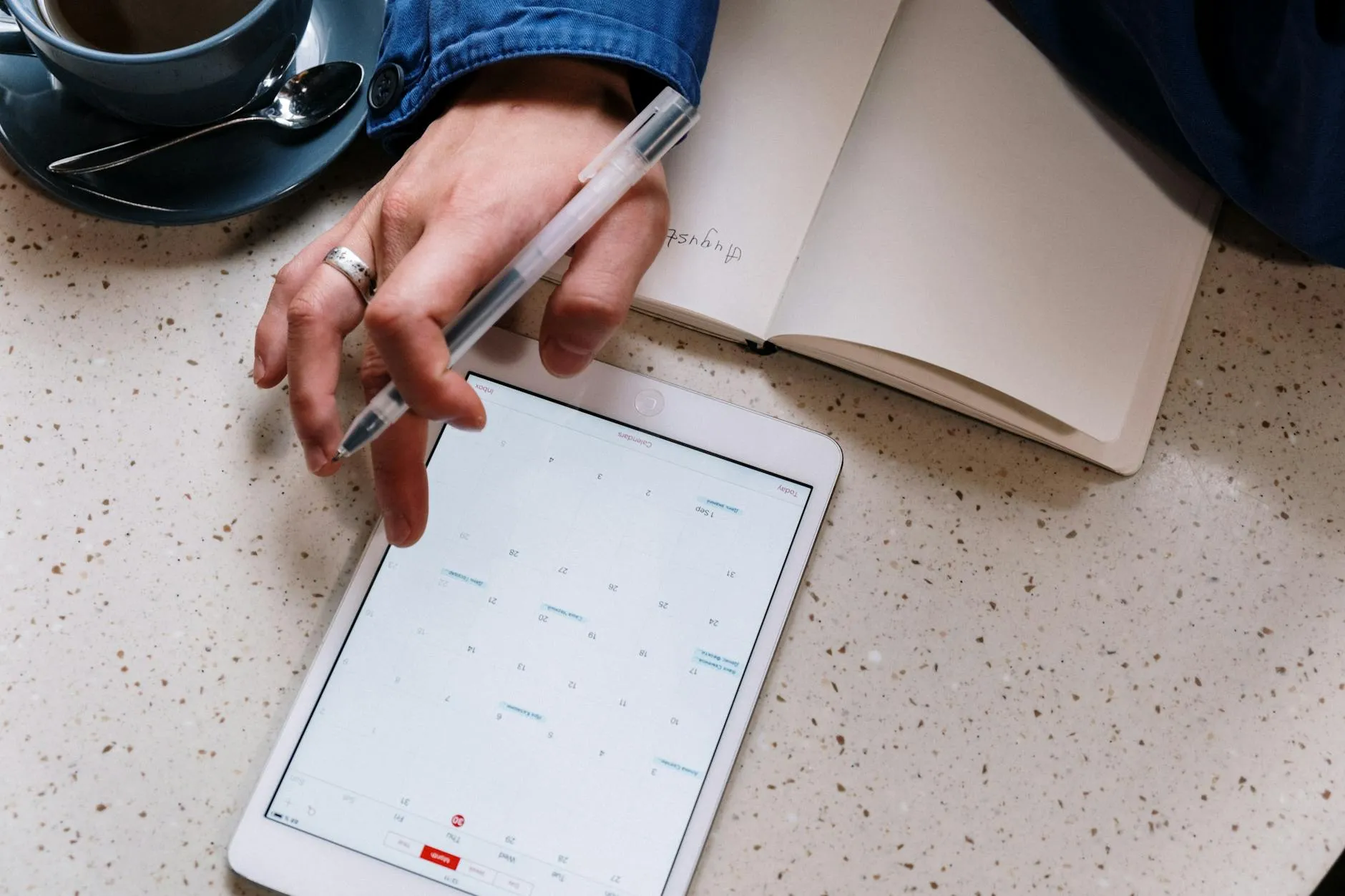 Close up shot of a student's hands writing tasks into a planner next to a tablet and a cup of coffee