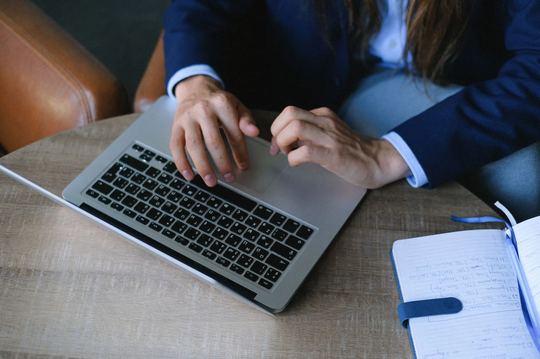 Close up of hands typing on a laptop keyboard next to a notebook with handwritten study notes