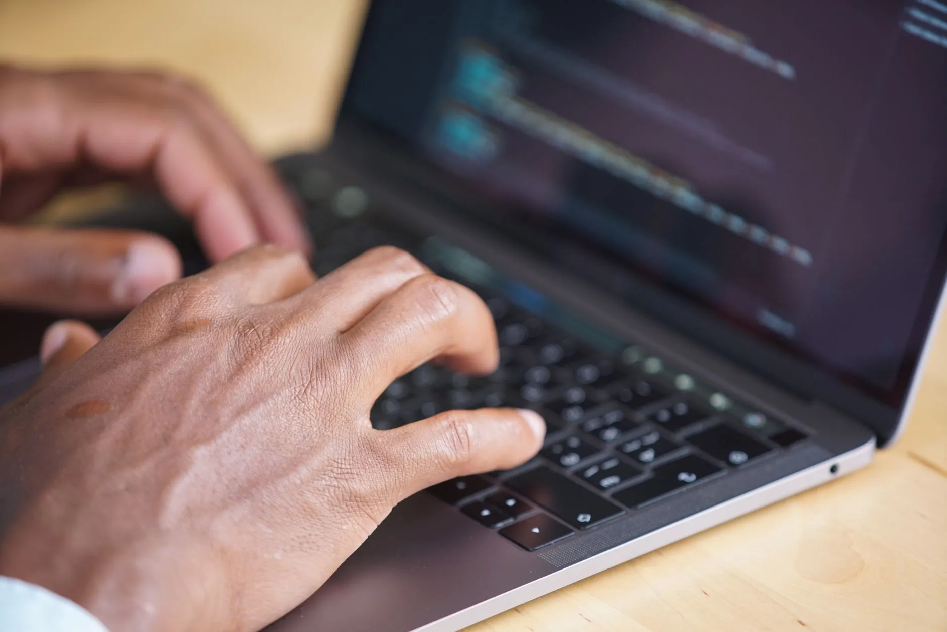 Close up of student hands typing notes on a laptop surrounded by books and a coffee cup on a wooden desk