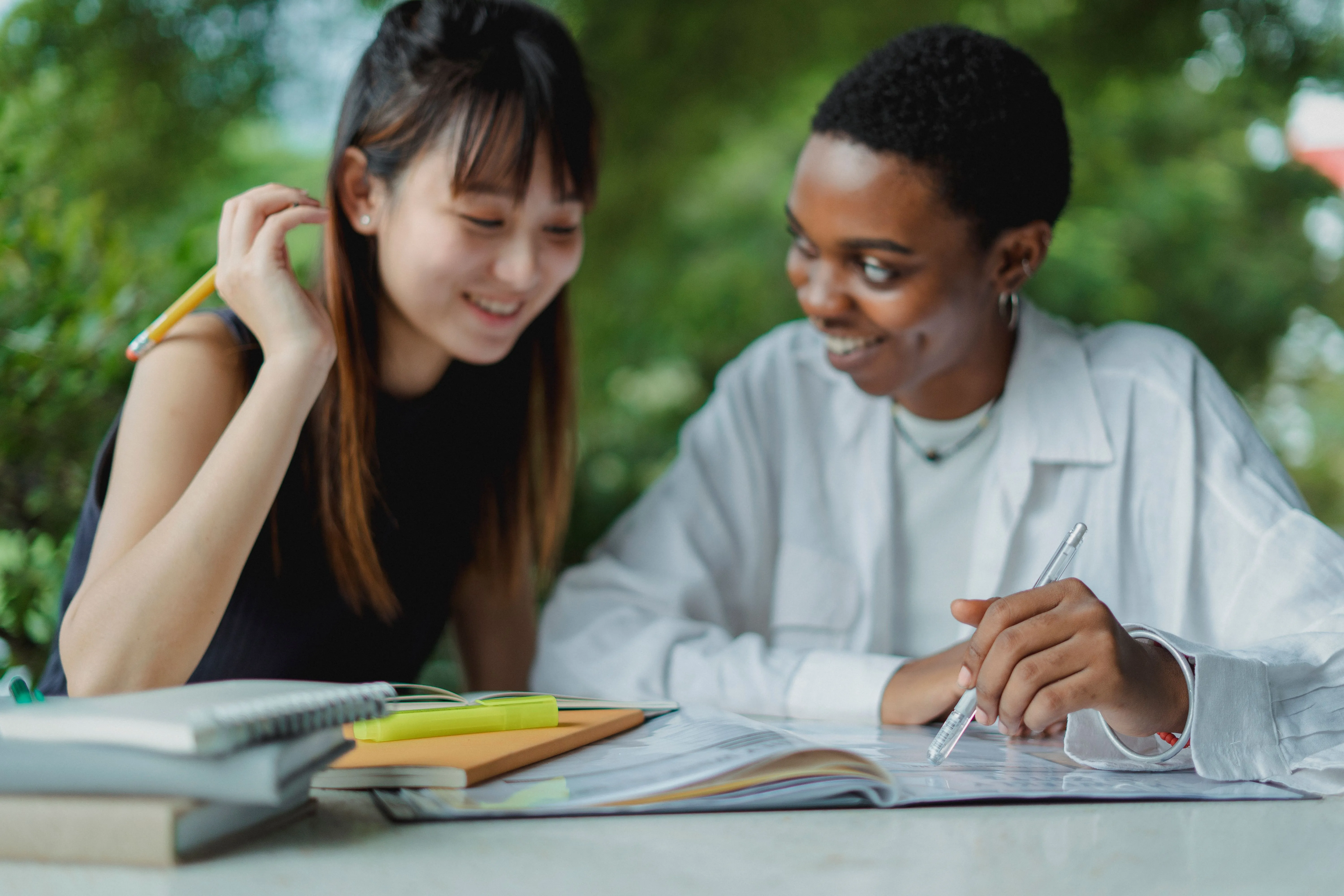 Smiling Asian and African American female students sitting at table and doing homework together