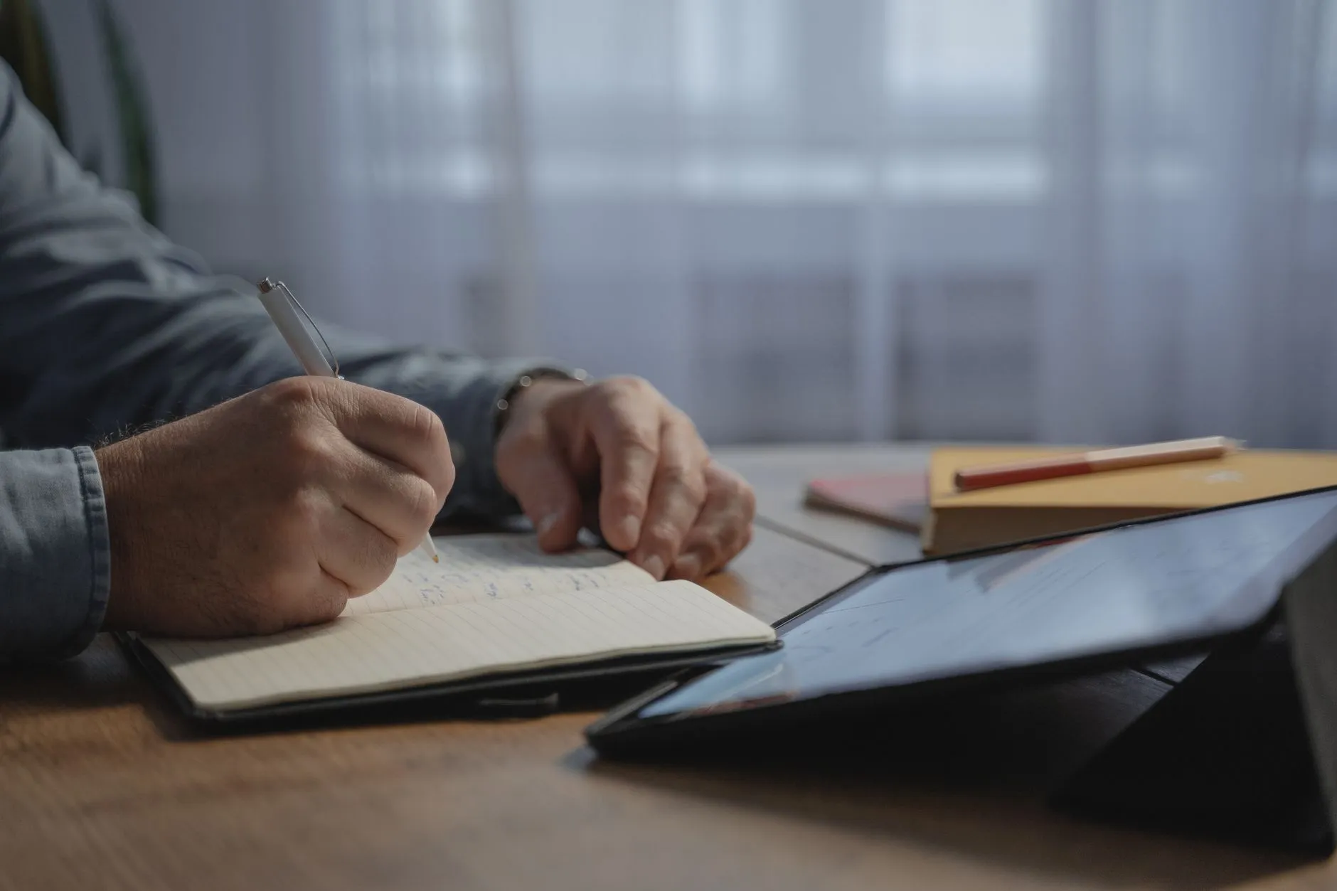 Close up of a student hands using a stylus to write notes on a tablet next to a laptop showing lecture slides
