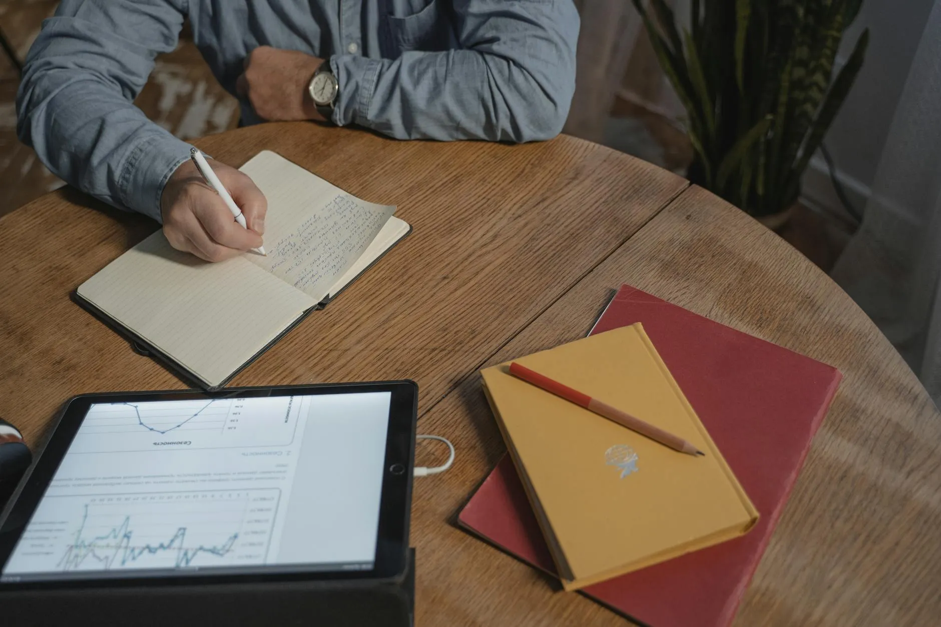 Close-up of student's hands creating digital flashcards on a tablet amidst a messy but cozy dorm room study desk.