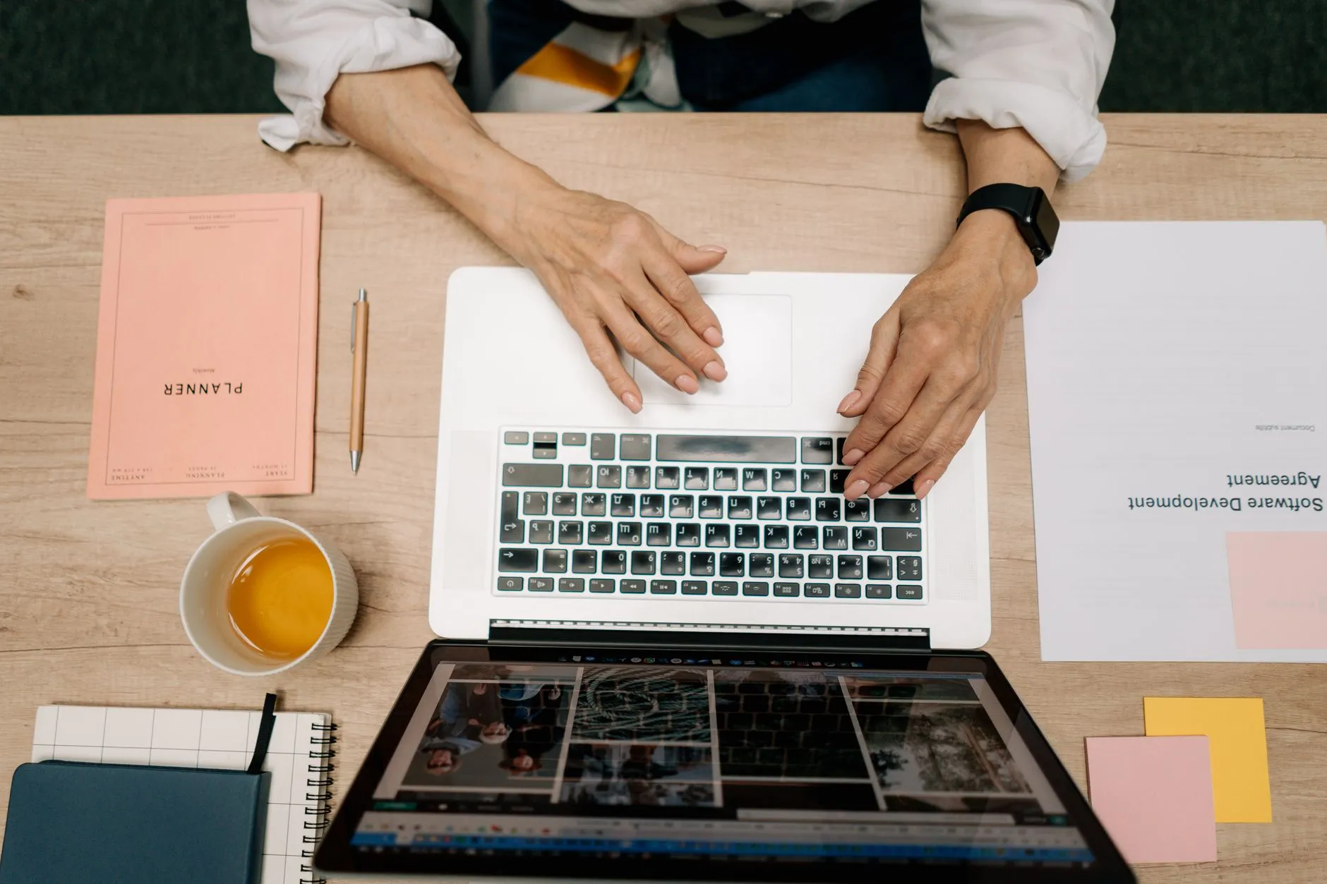 Close up of student hands typing on a laptop next to a messy study desk with notebooks