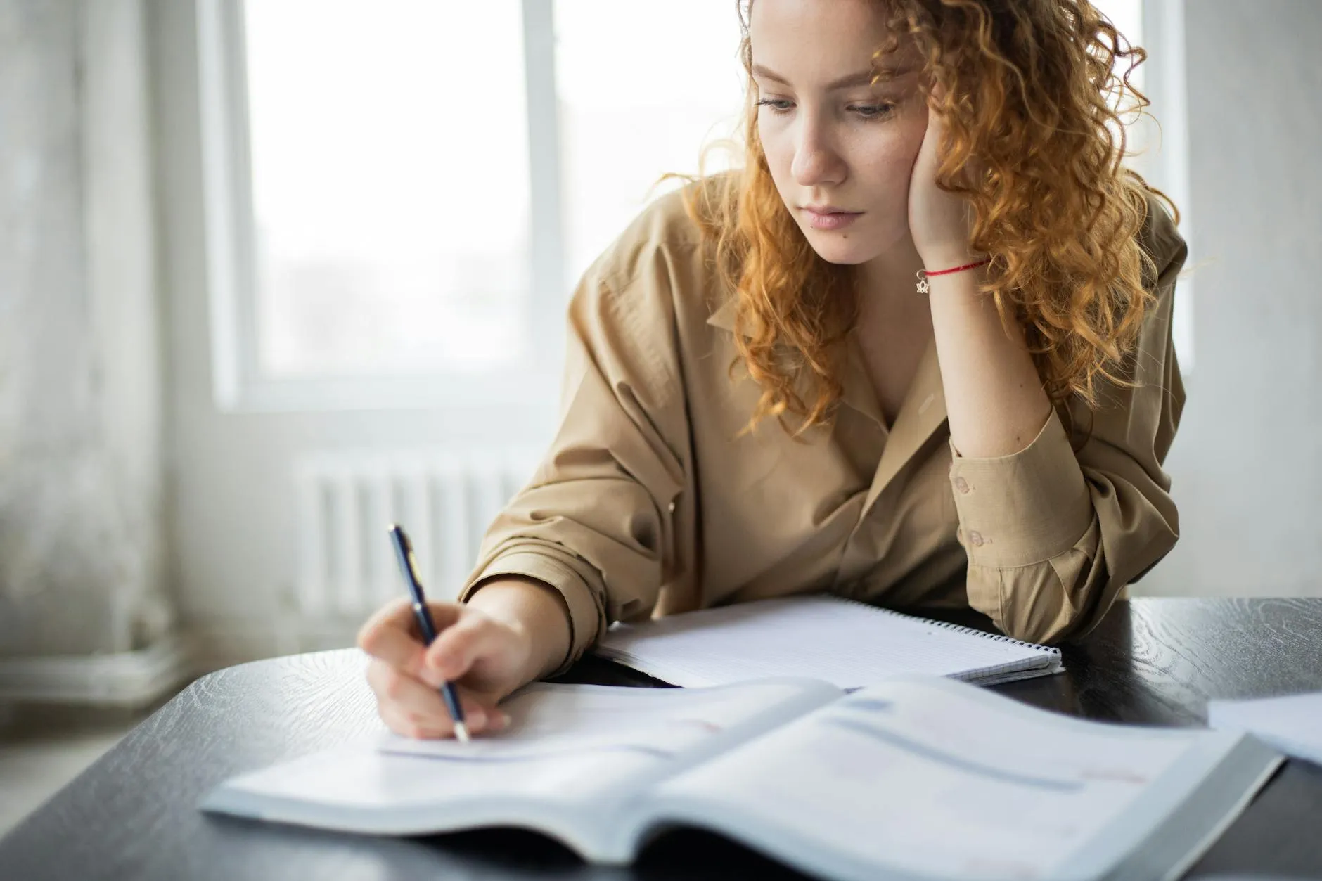 Close-up of a student's hands using a tablet to create flashcards on a messy dorm room desk.
