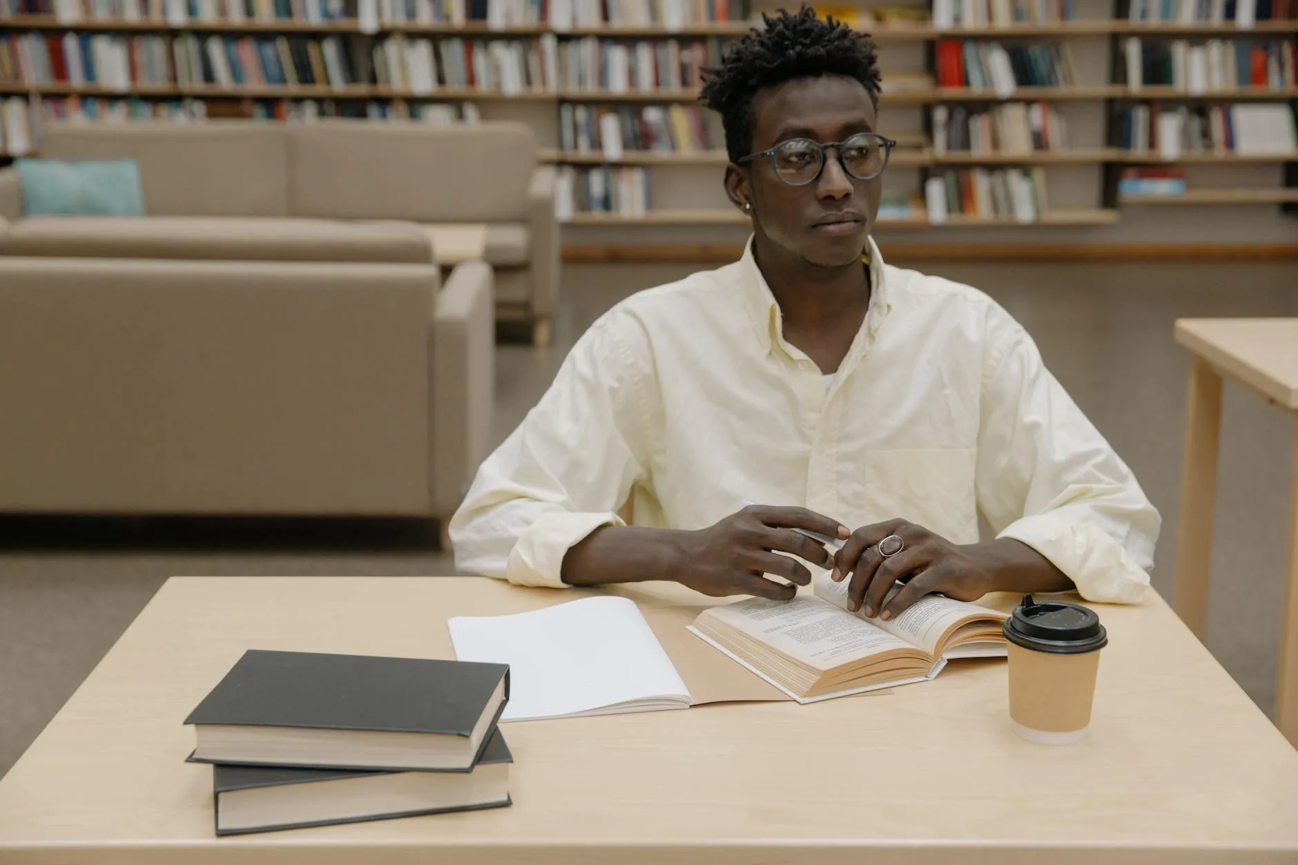 A student holding a warm coffee cup at a wooden library desk with books in the background