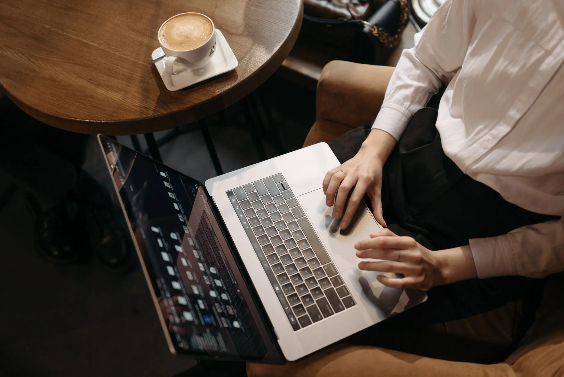 Close up of a student typing on a laptop with study notes and a coffee cup on a wooden desk