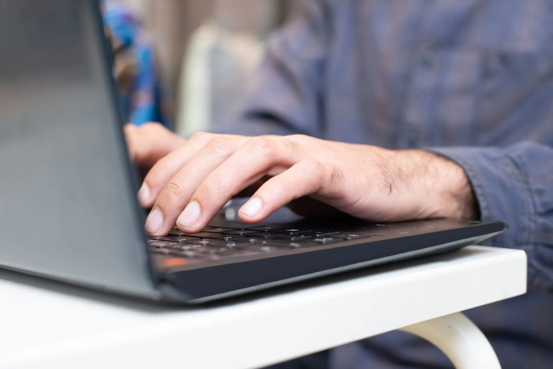 Close up of hands typing notes on a laptop surrounded by textbooks and coffee