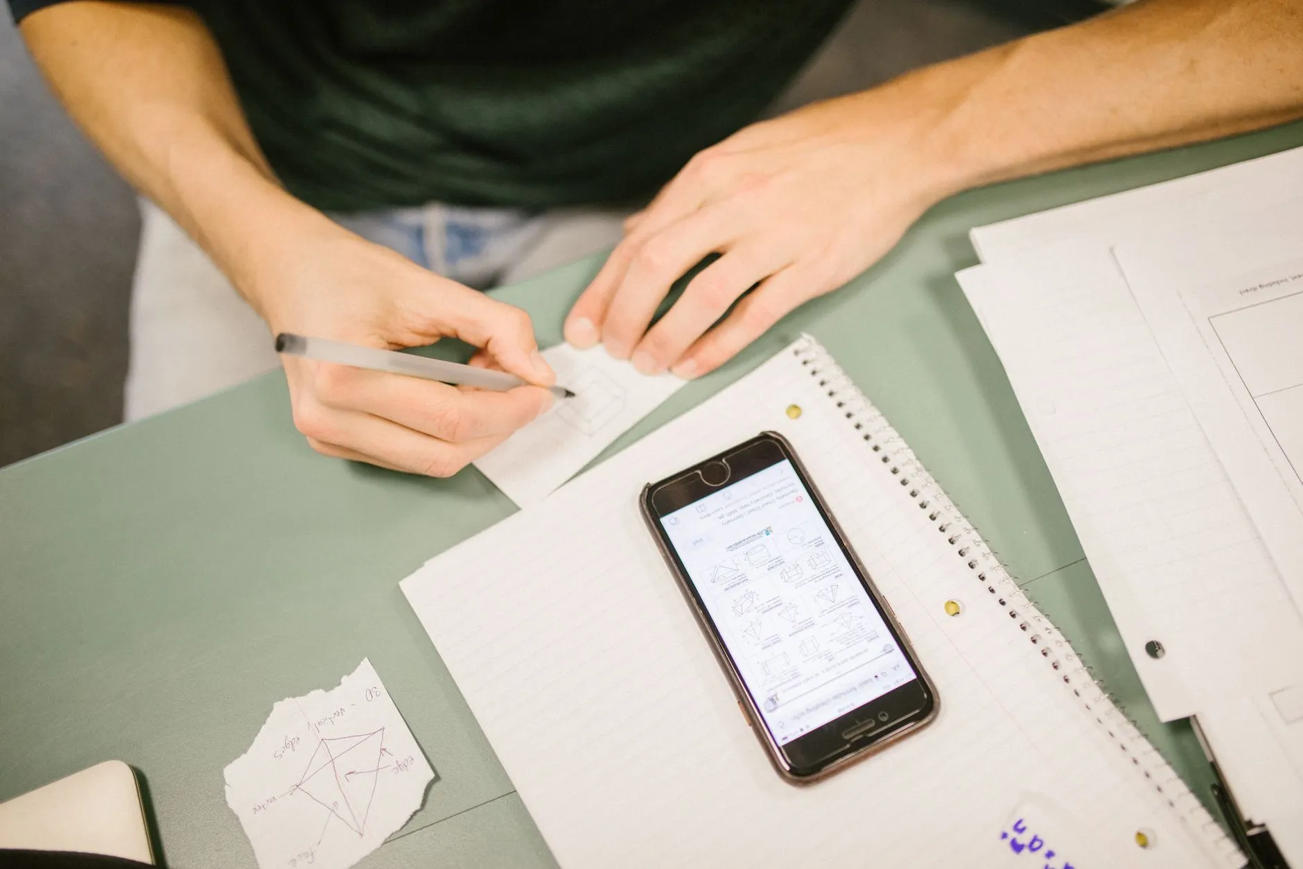 Close up of hands using a tablet to create digital flashcards on a messy dorm room desk