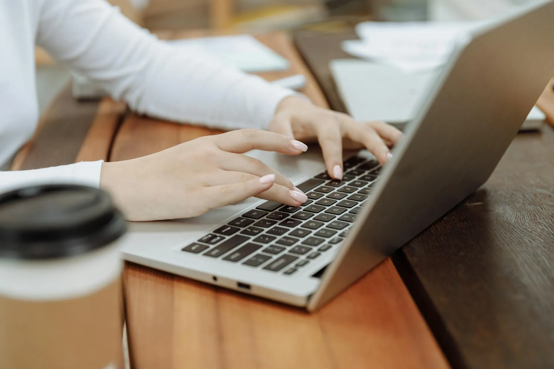 A close-up shot of a student's hands typing on a laptop in a busy campus coffee shop with a latte nearby