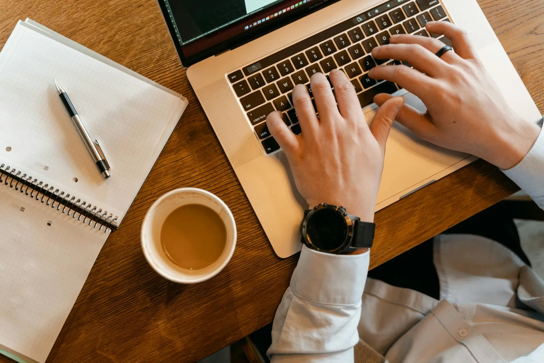 A detailed shot of a student's hands typing on a laptop next to a cup of coffee and organized study notes