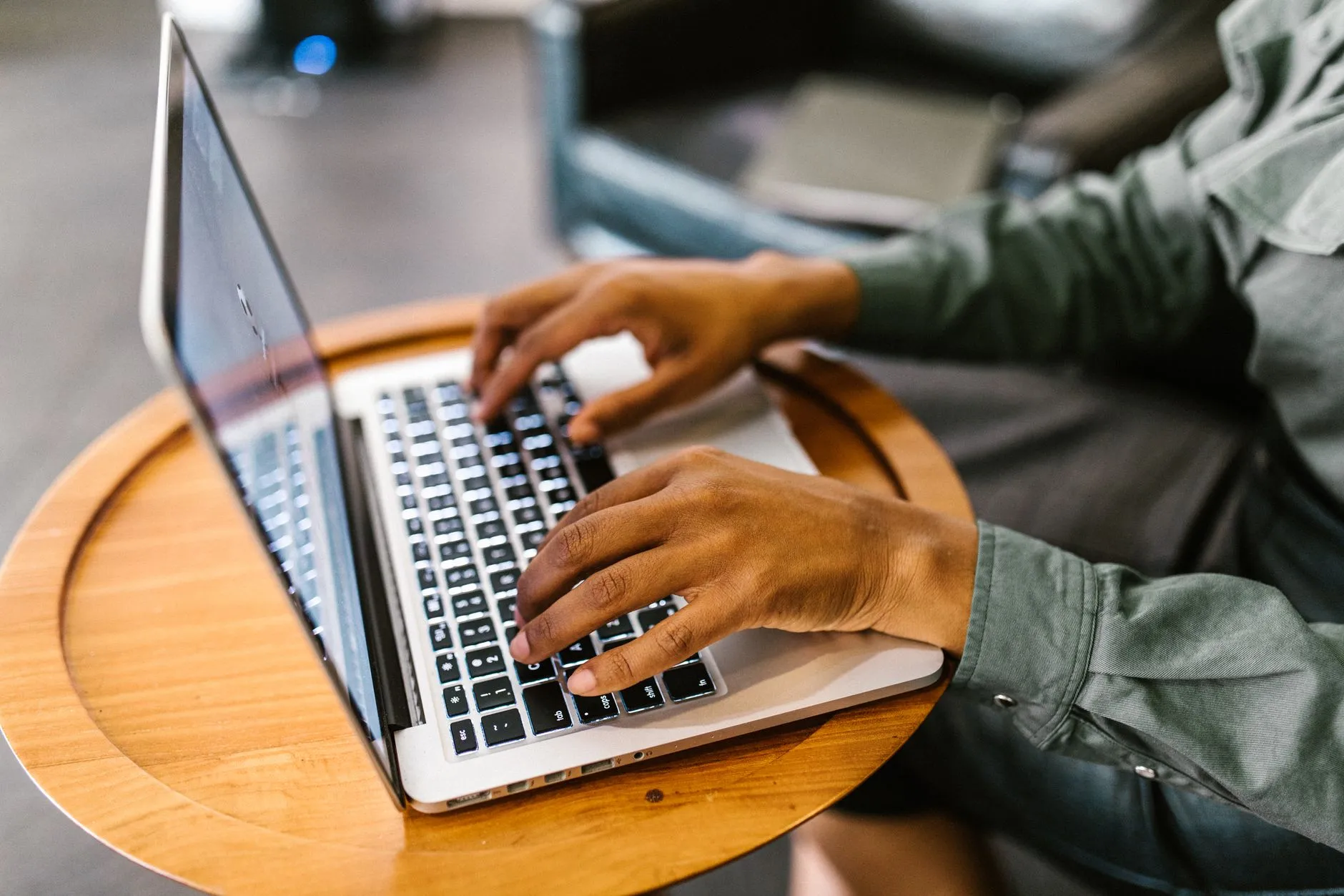 Close up of hands typing on a laptop keyboard on a messy study desk with a coffee cup