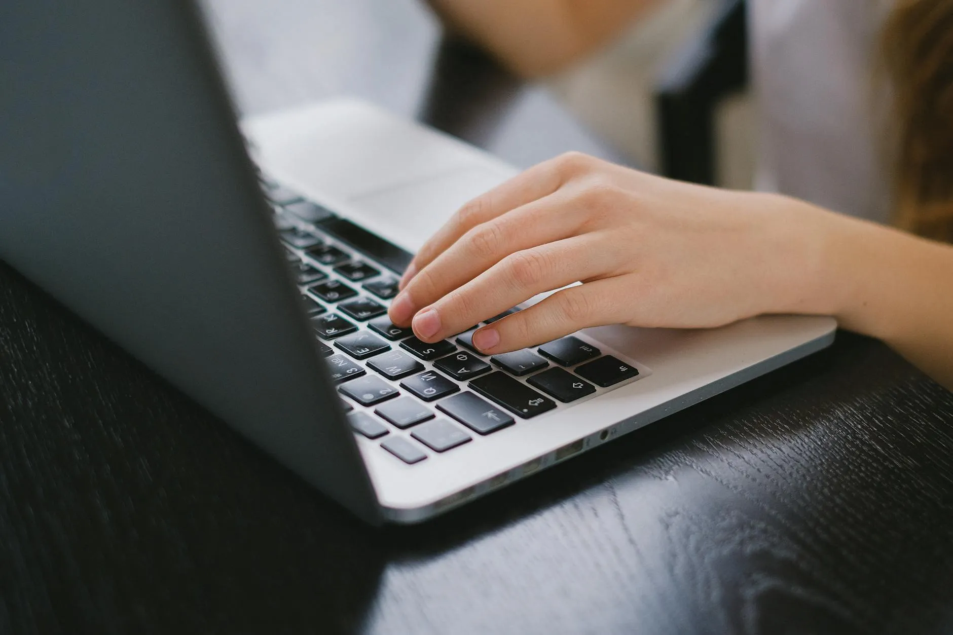 Close up of a student typing notes on a laptop at a messy wooden desk with coffee