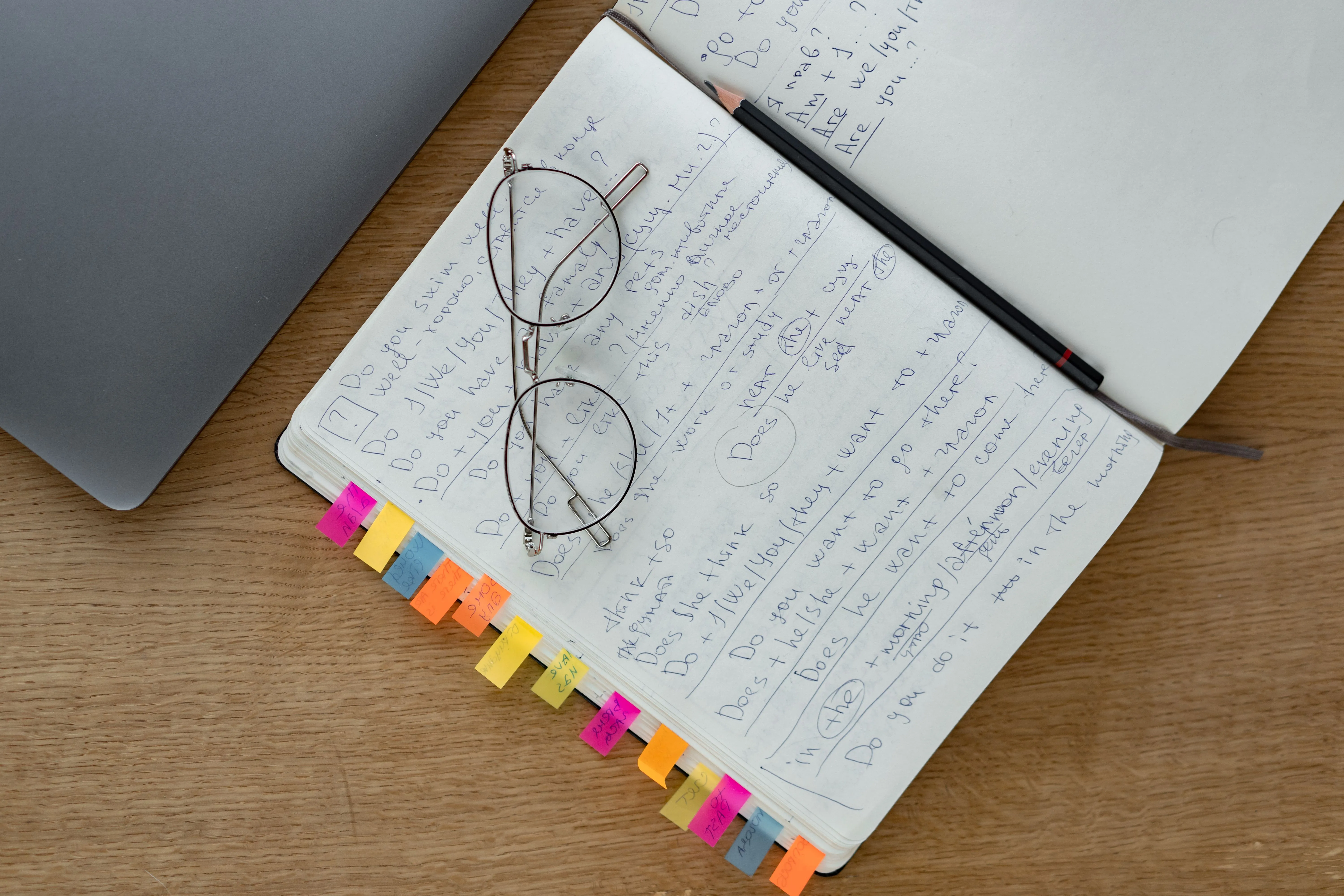 Top view of a notebook with handwritten notes, eyeglasses, and a pencil on a wooden desk.