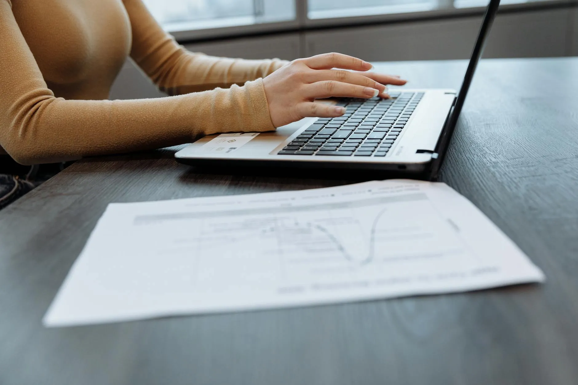Close-up of student's hands typing a detailed AI prompt on a laptop keyboard