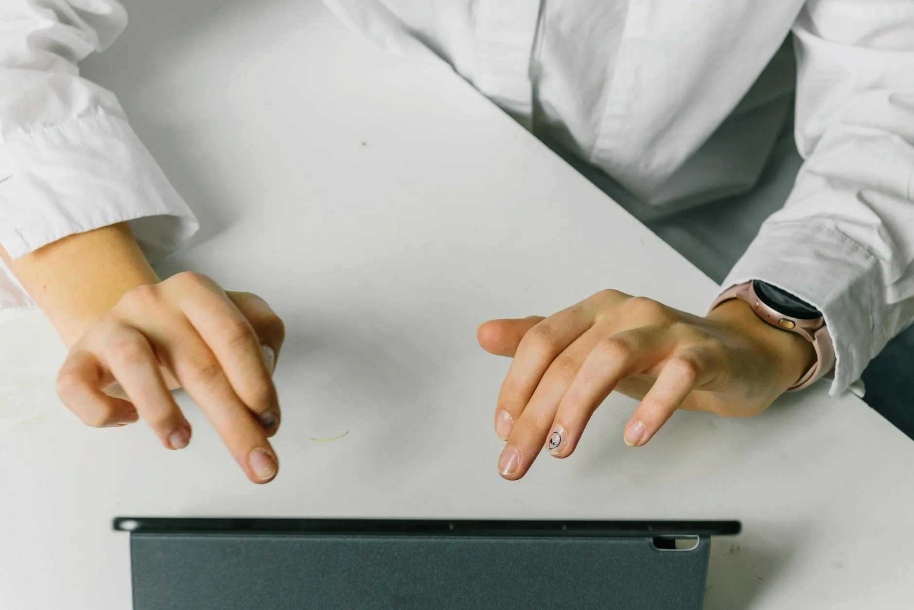 Close up of student hands typing on a tablet at a messy study desk with a coffee cup