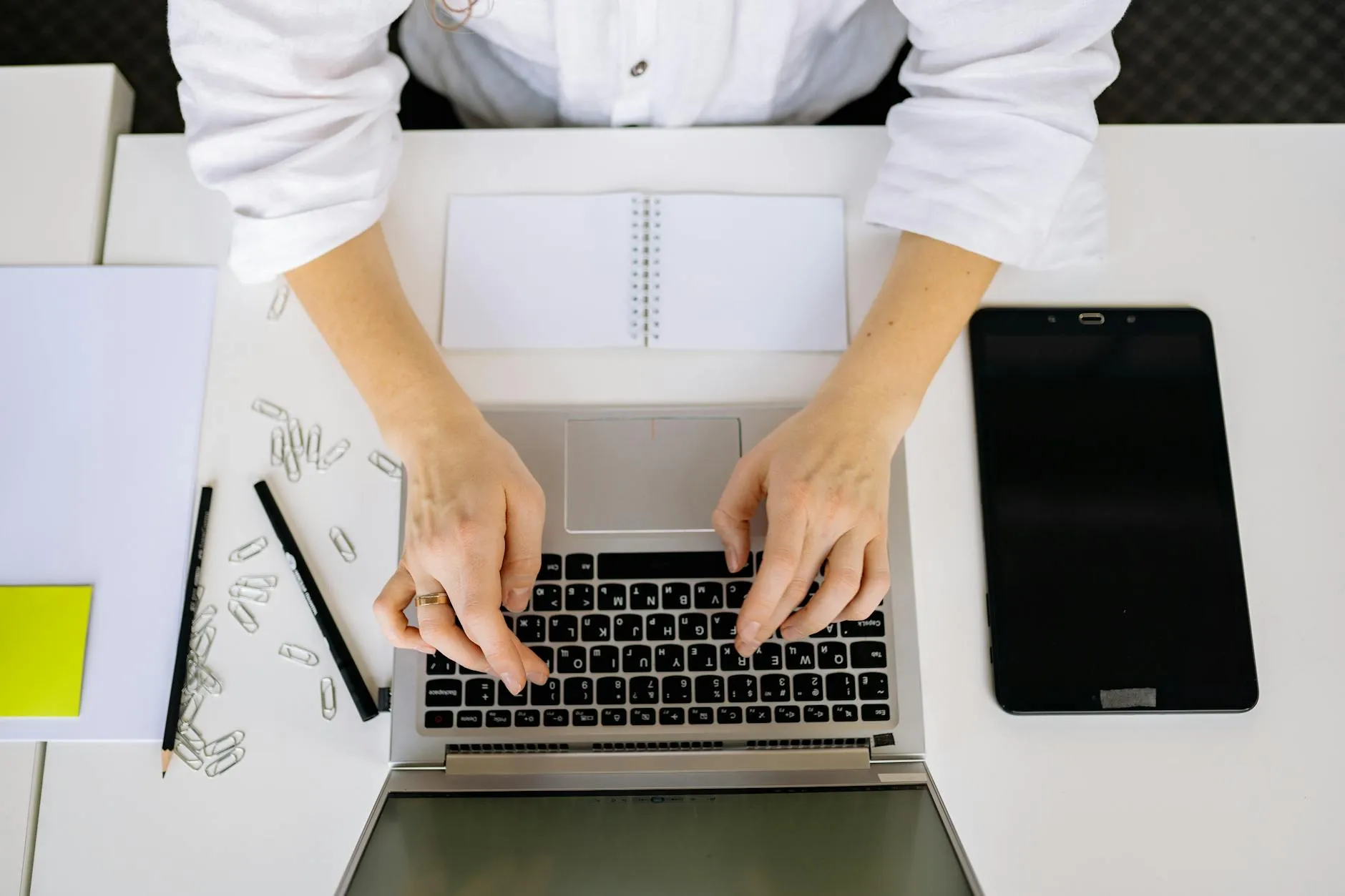Close up of a student typing on a laptop at a messy desk with notebooks and pens