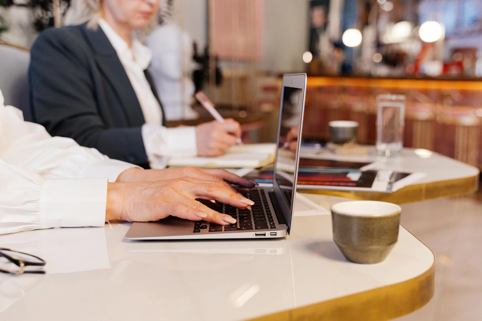 Close up of student hands typing on a laptop next to a notebook on a messy study desk