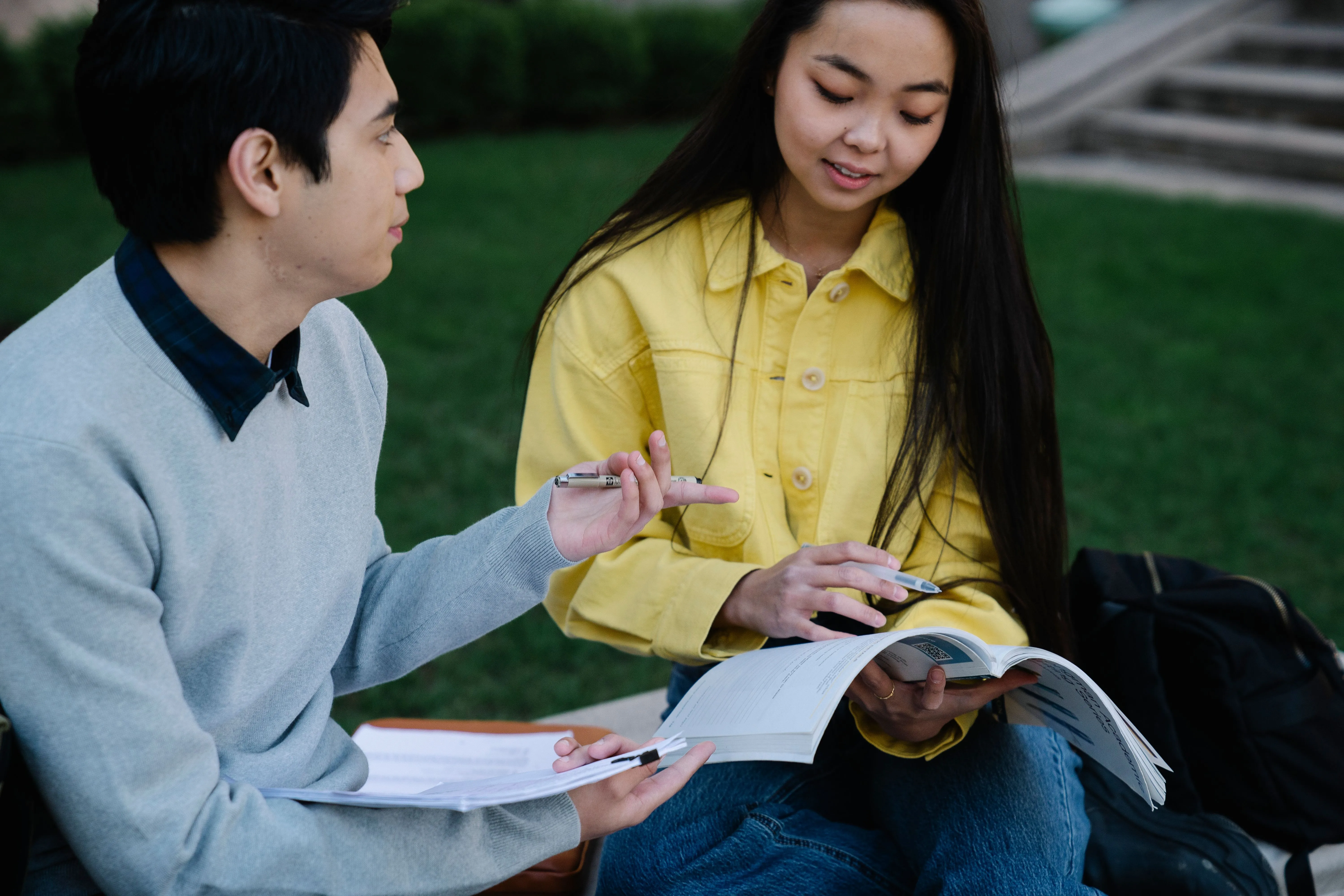Two students engage in outdoor study session with textbooks and notes.