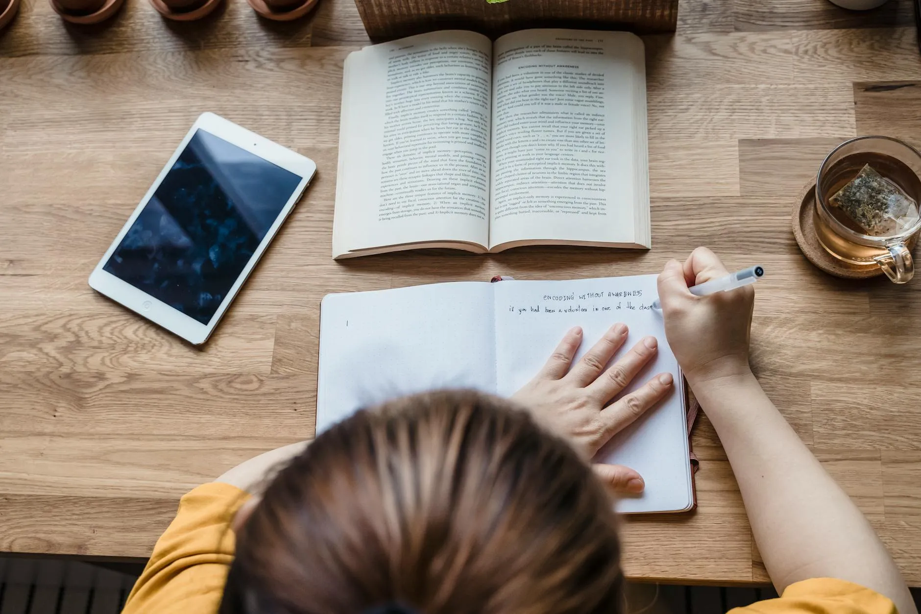 Close up of a student using a tablet to organize study notes on a messy dorm room desk