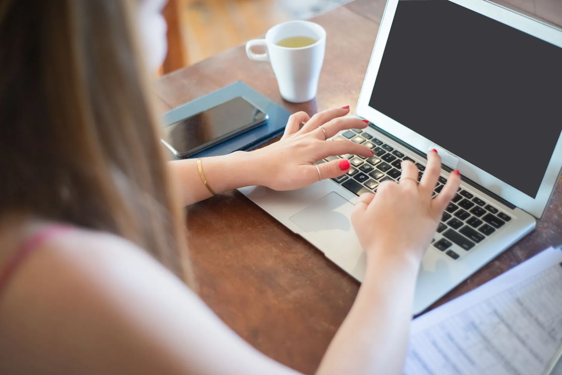Close up of hands typing on a laptop on a messy student desk with a coffee cup