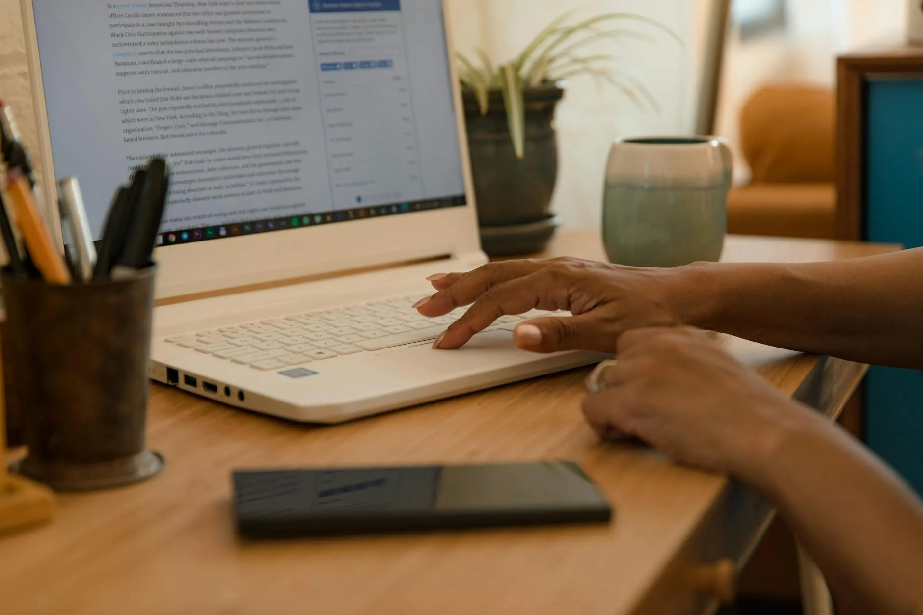 Close up of a student's hands working on a laptop at a messy dorm desk with a coffee cup