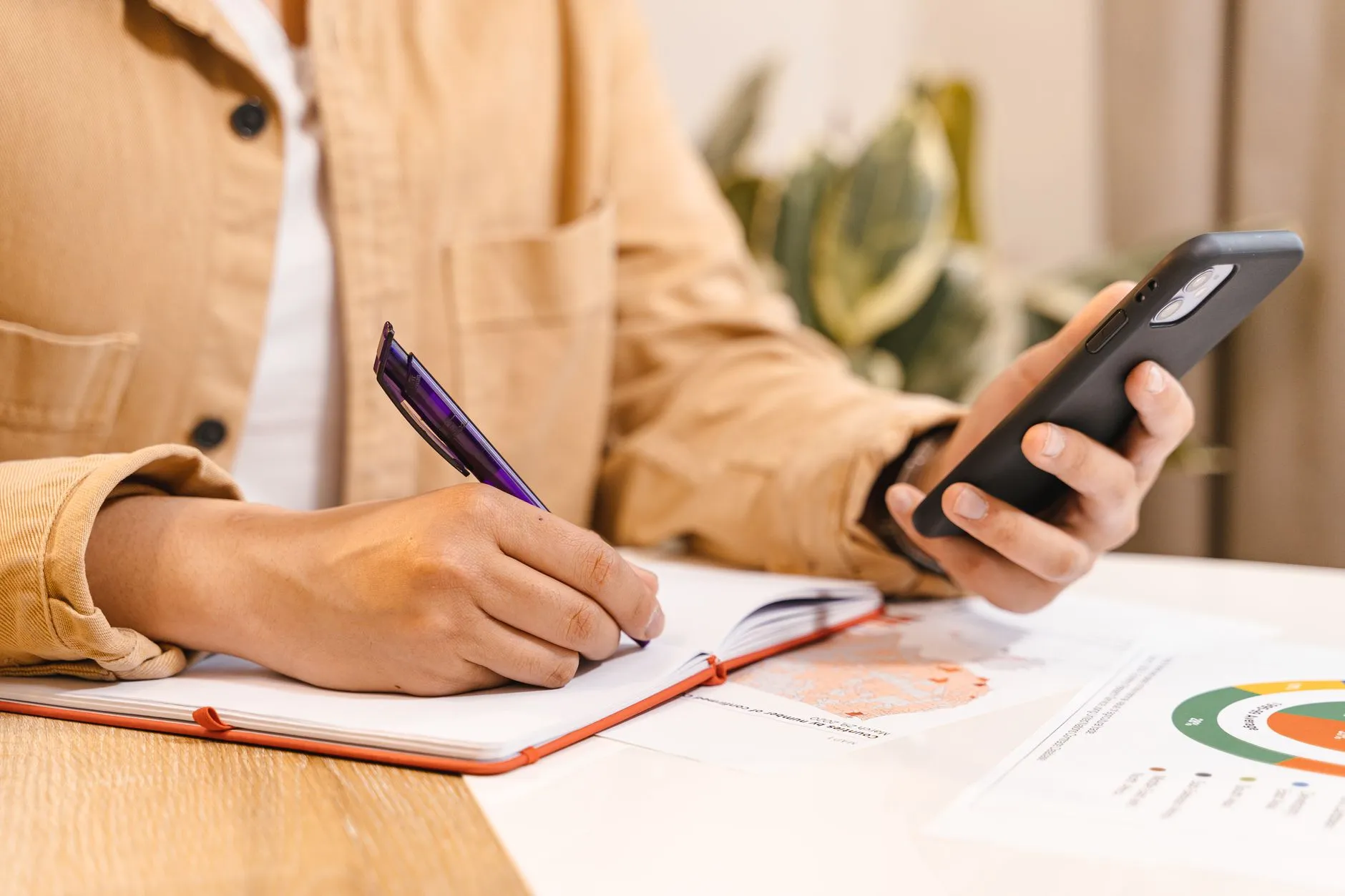 Close up of student hands writing notes next to a tablet displaying presentation slides