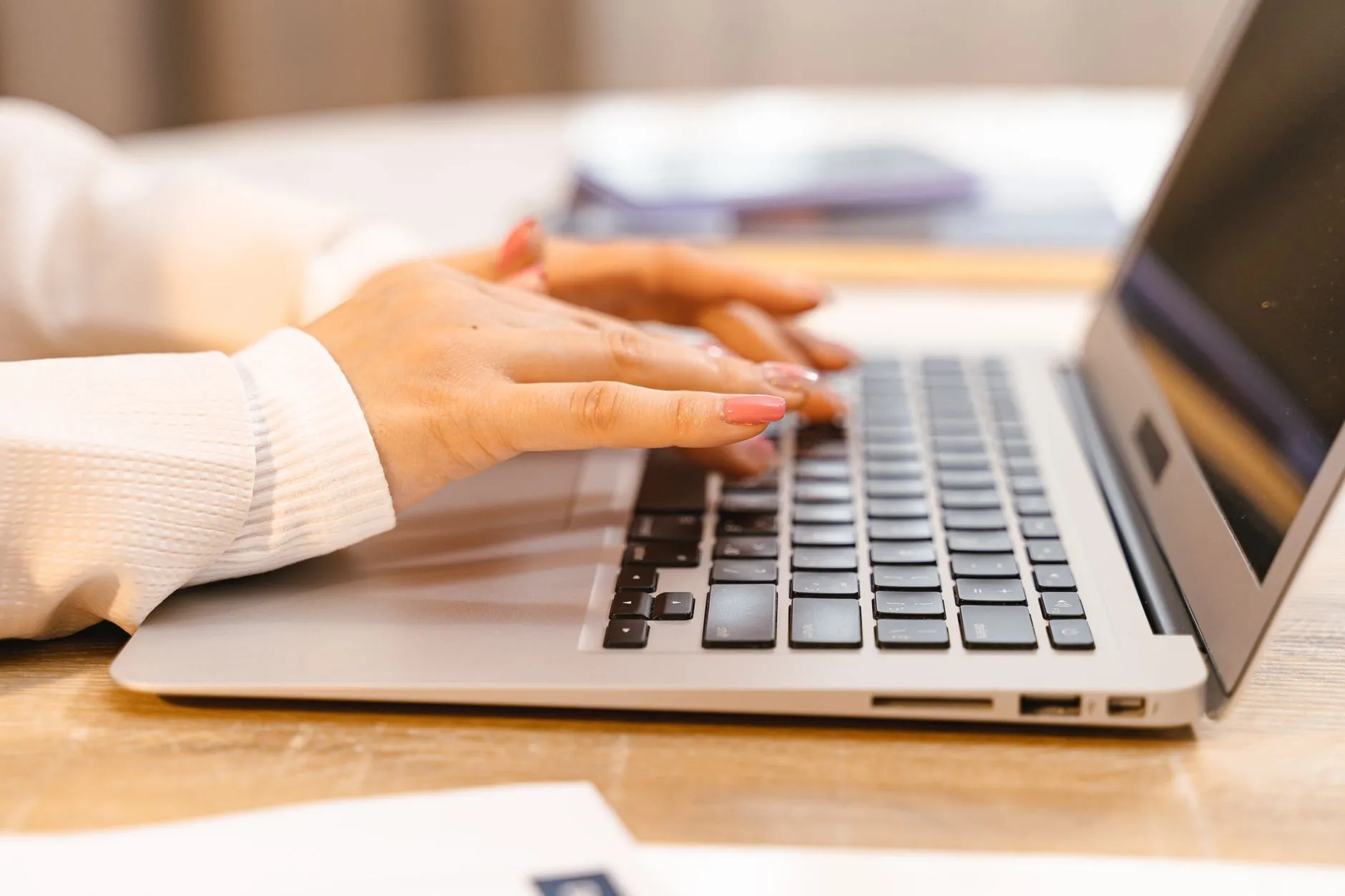 Close up of a student typing on a laptop surrounded by notebooks and coffee on a messy desk