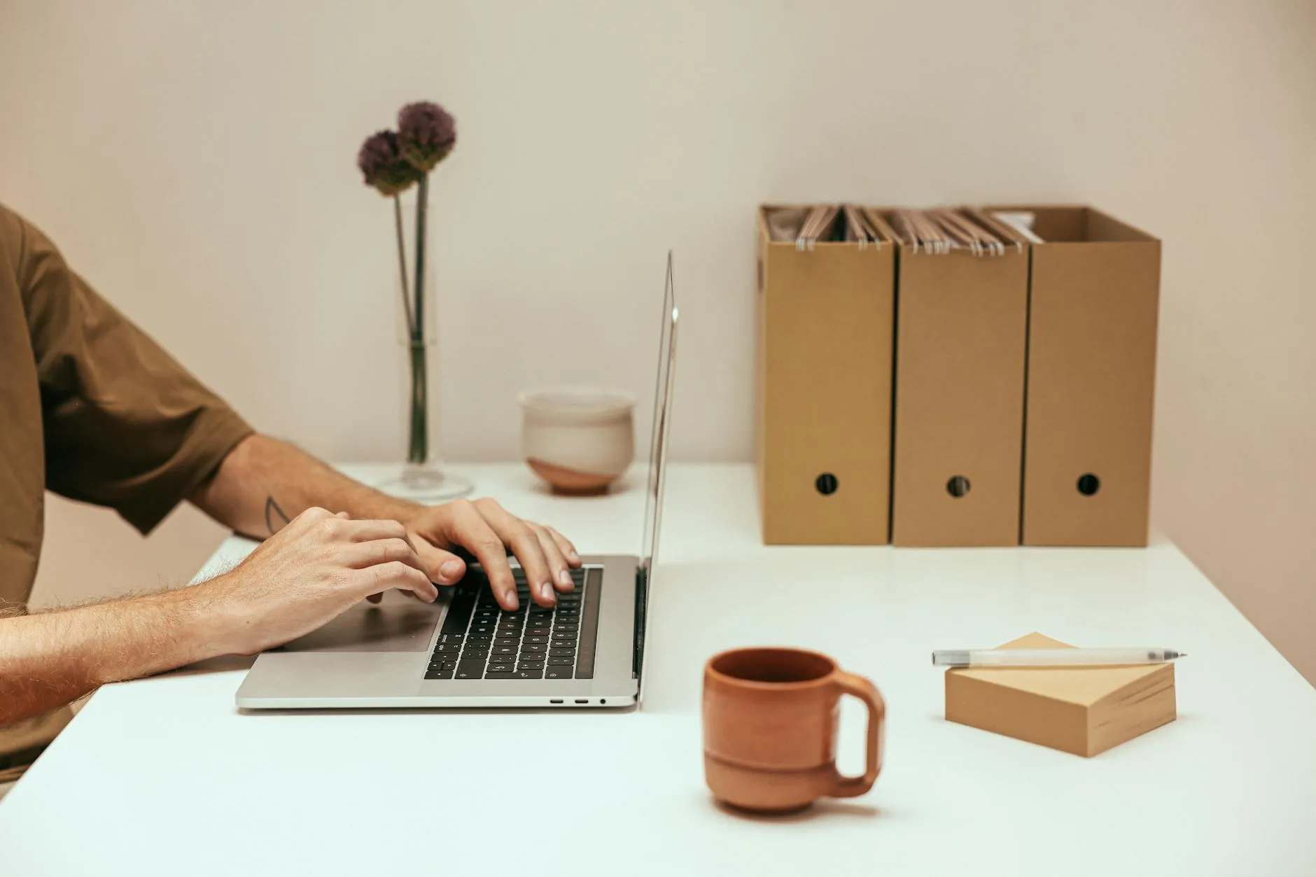 Close up of a student's hands typing on a laptop on a messy dorm room desk with coffee and notebooks