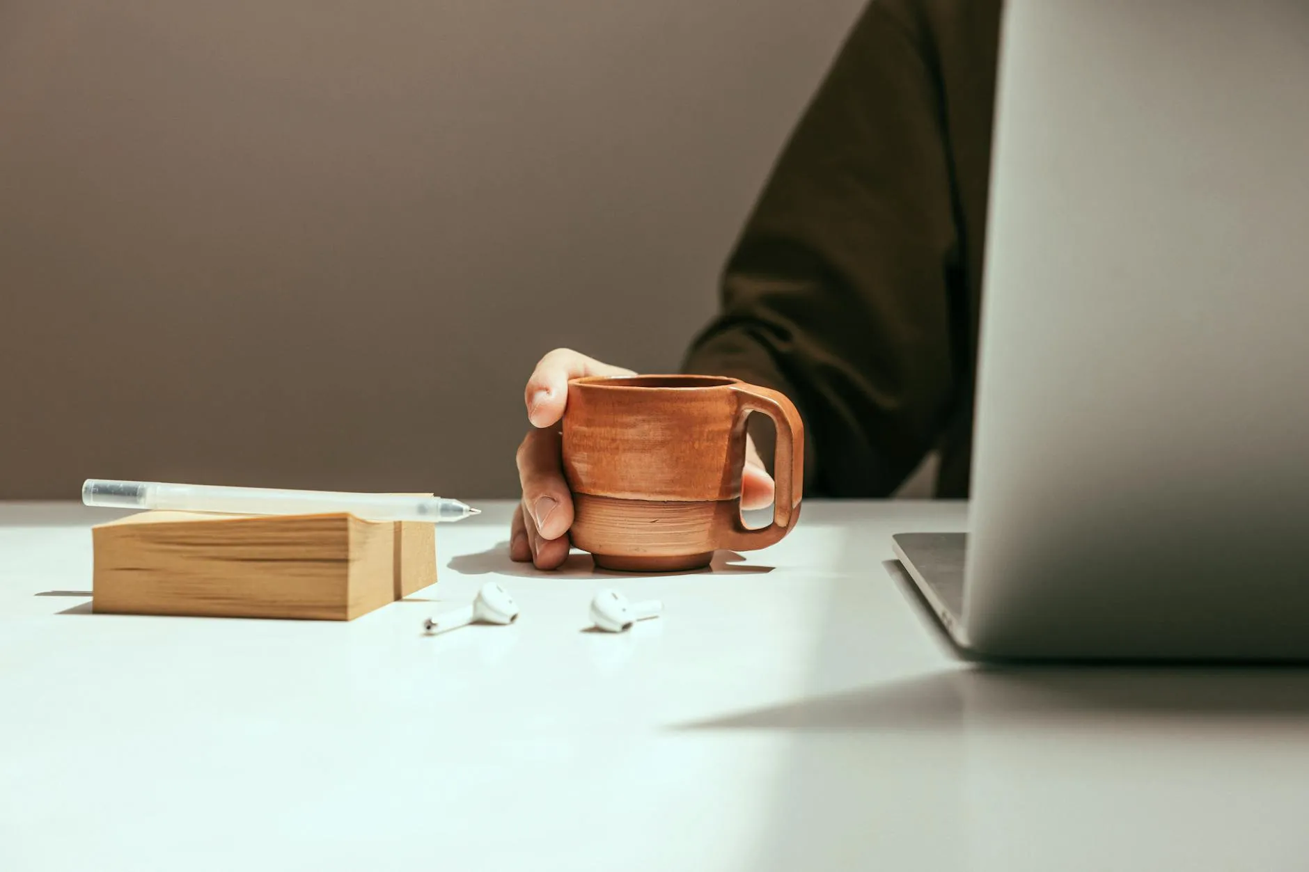 A close up of a student's hands holding a coffee mug over a messy desk with study materials