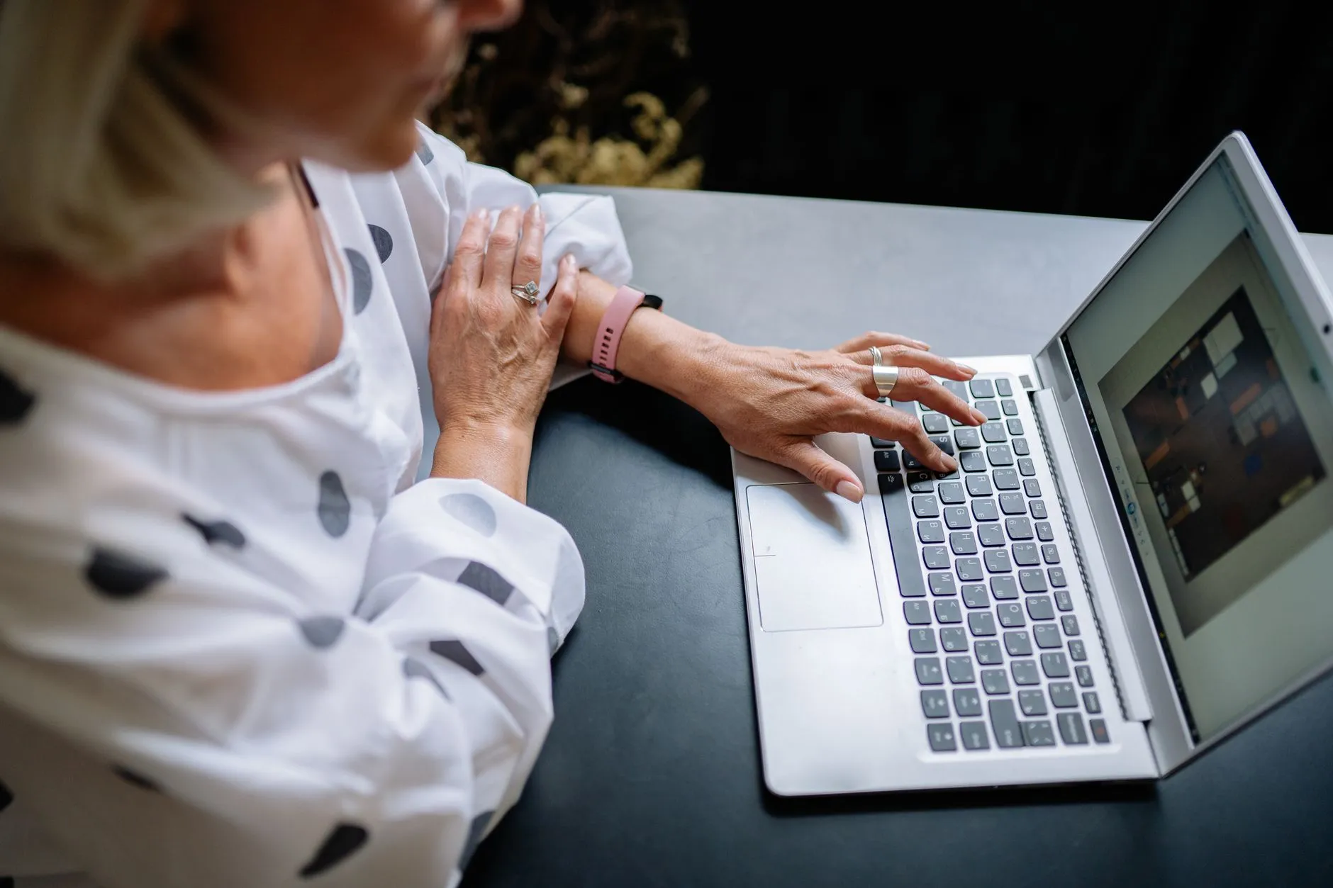 Close up of hands typing on a laptop on a wooden desk in a cozy university library with soft lighting