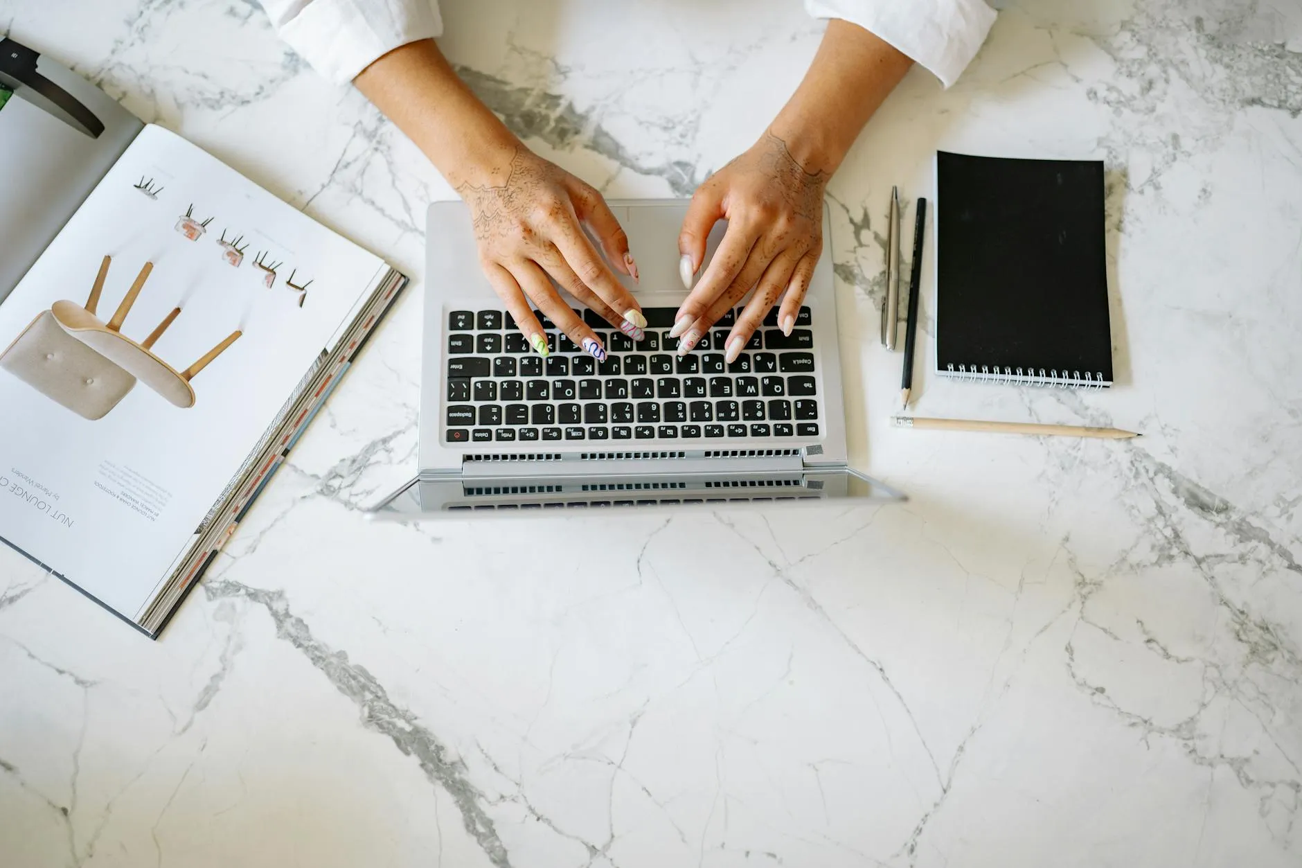 Close up of student hands typing on a laptop next to an open notebook on a messy study desk