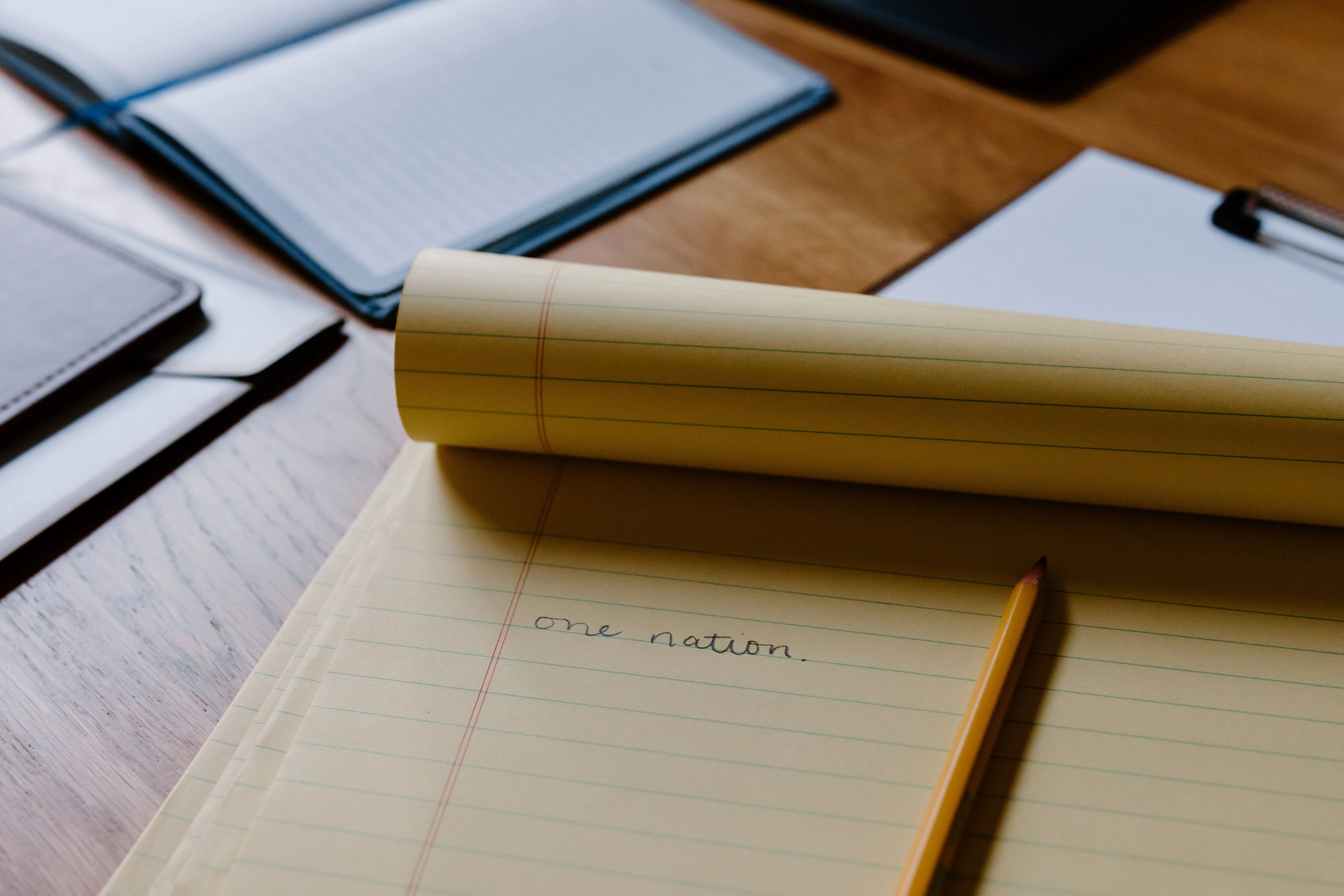 Close-up of a handwritten note on a yellow notepad, featuring the phrase 'one nation' with a pencil nearby.