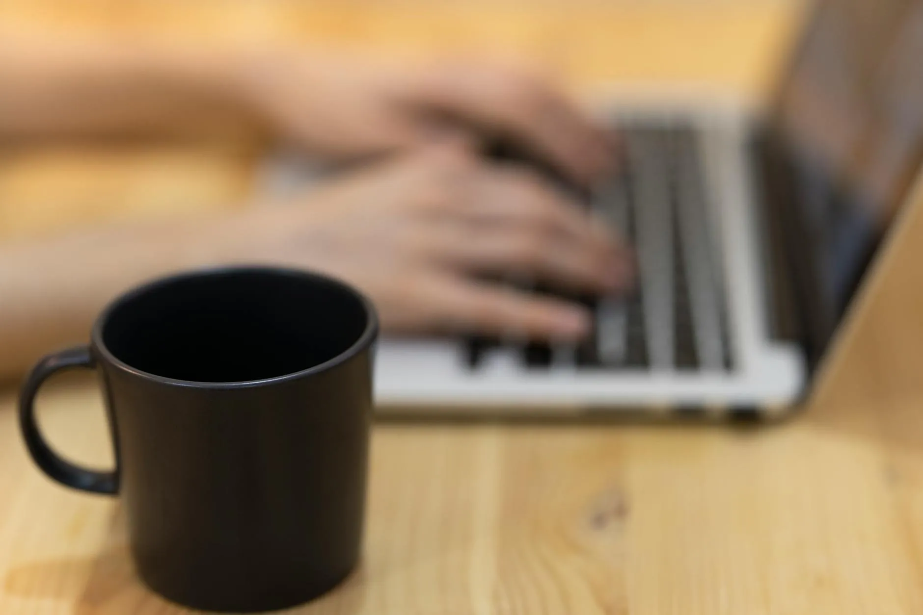 Detail shot of a student typing on a laptop next to a coffee cup on a wooden desk
