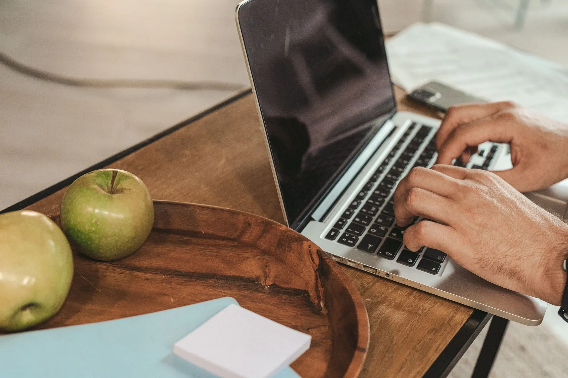 Close up of hands typing on a laptop on a messy student desk with a coffee cup and notebooks